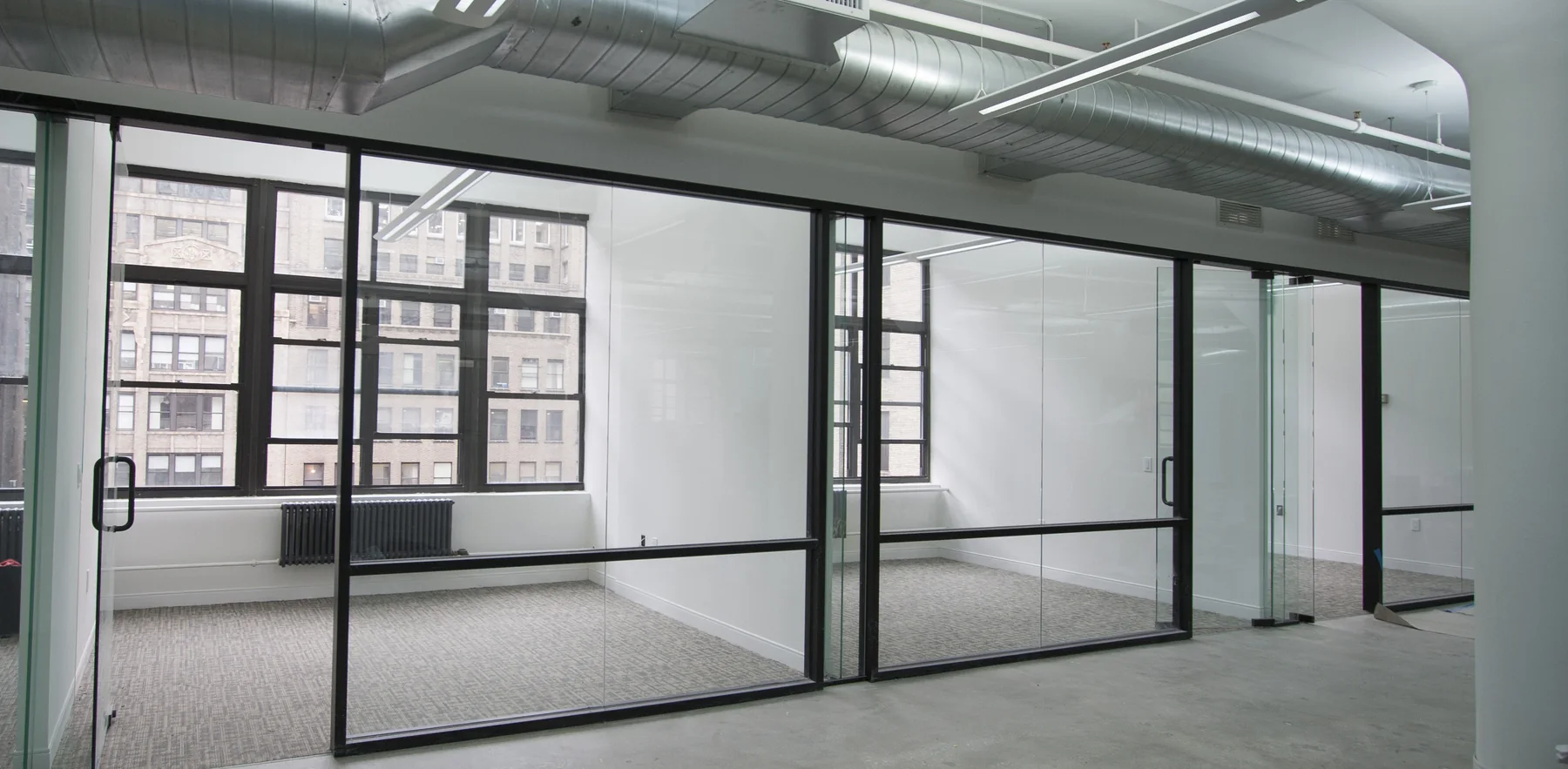 Glass-front private offices with exposed ductwork in a New York commercial interior