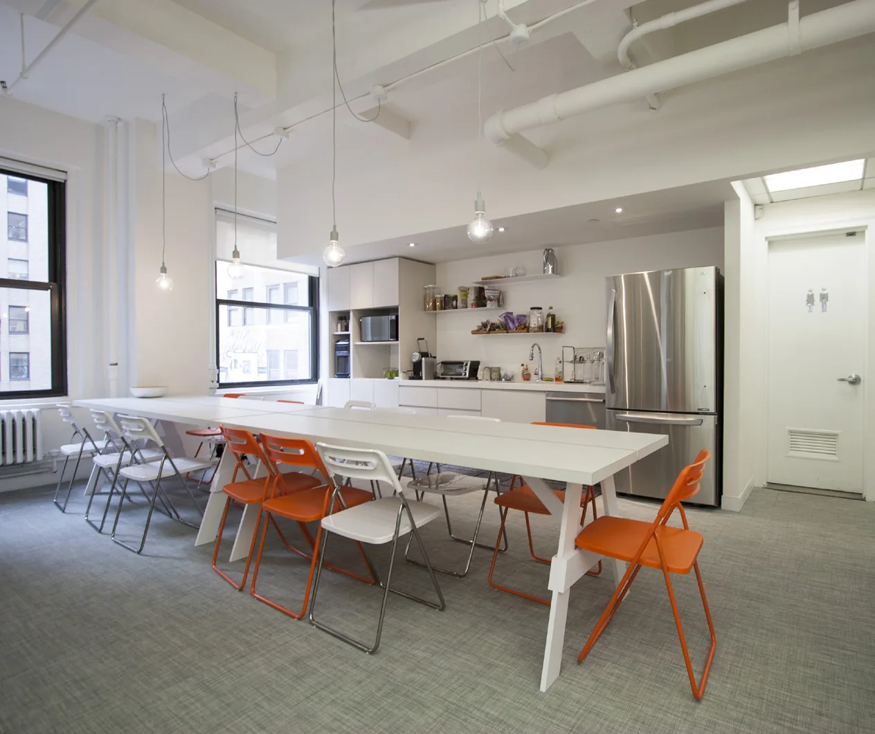 Bright workplace pantry with a long communal table and orange chairs