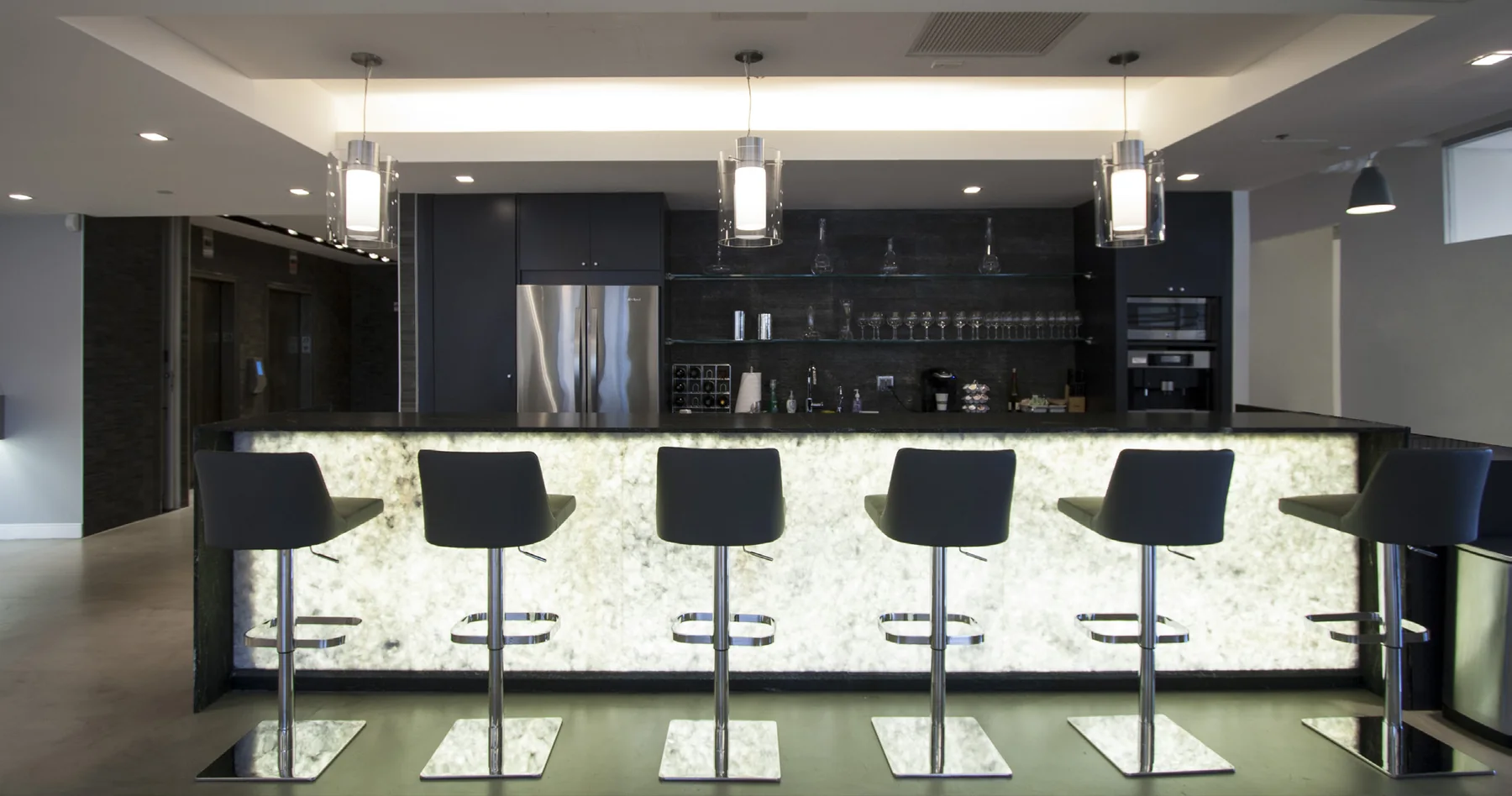 Illuminated stone bar and dark cabinetry in a workplace lounge